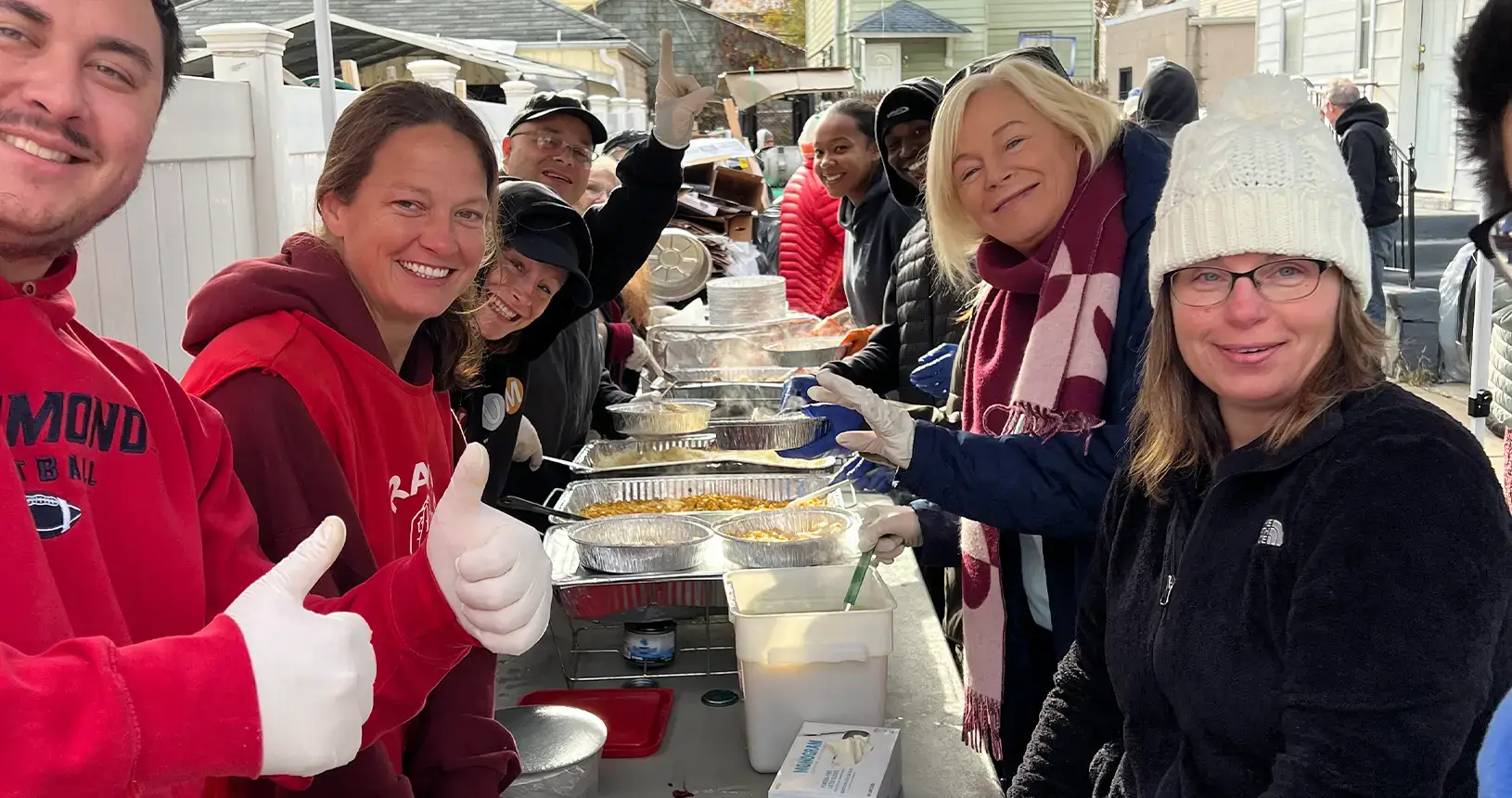 Volunteers smiling and giving a thumbs up while serving Thanksgiving dinner from metal trays