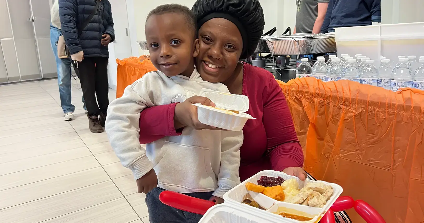 A mother and her young son smiling, holding their Thanksgiving dinner at an Operation Drumstick outreach