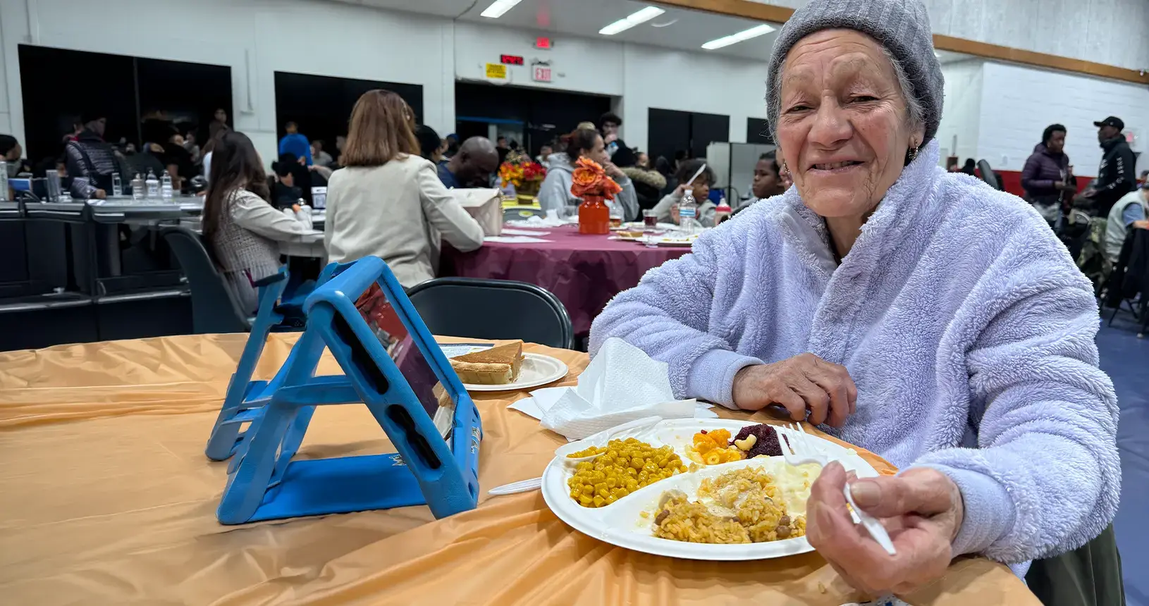 A smiling older woman enjoying Thanksgiving dinner at an Operation Drumstick outreach